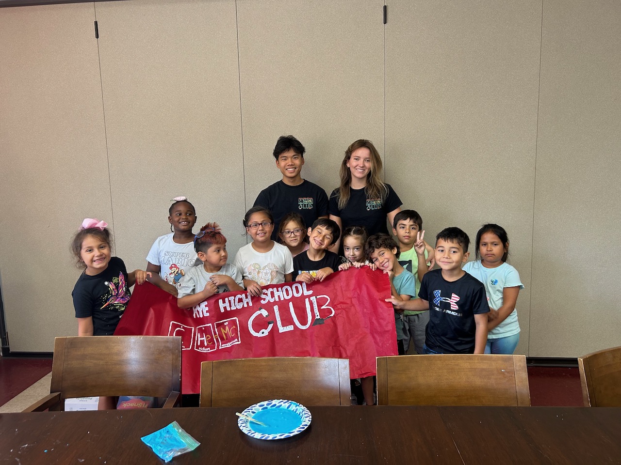 Chemistry Club volunteers and children holding the Rye High School Chem Club banner at Don Bosco Community Center.