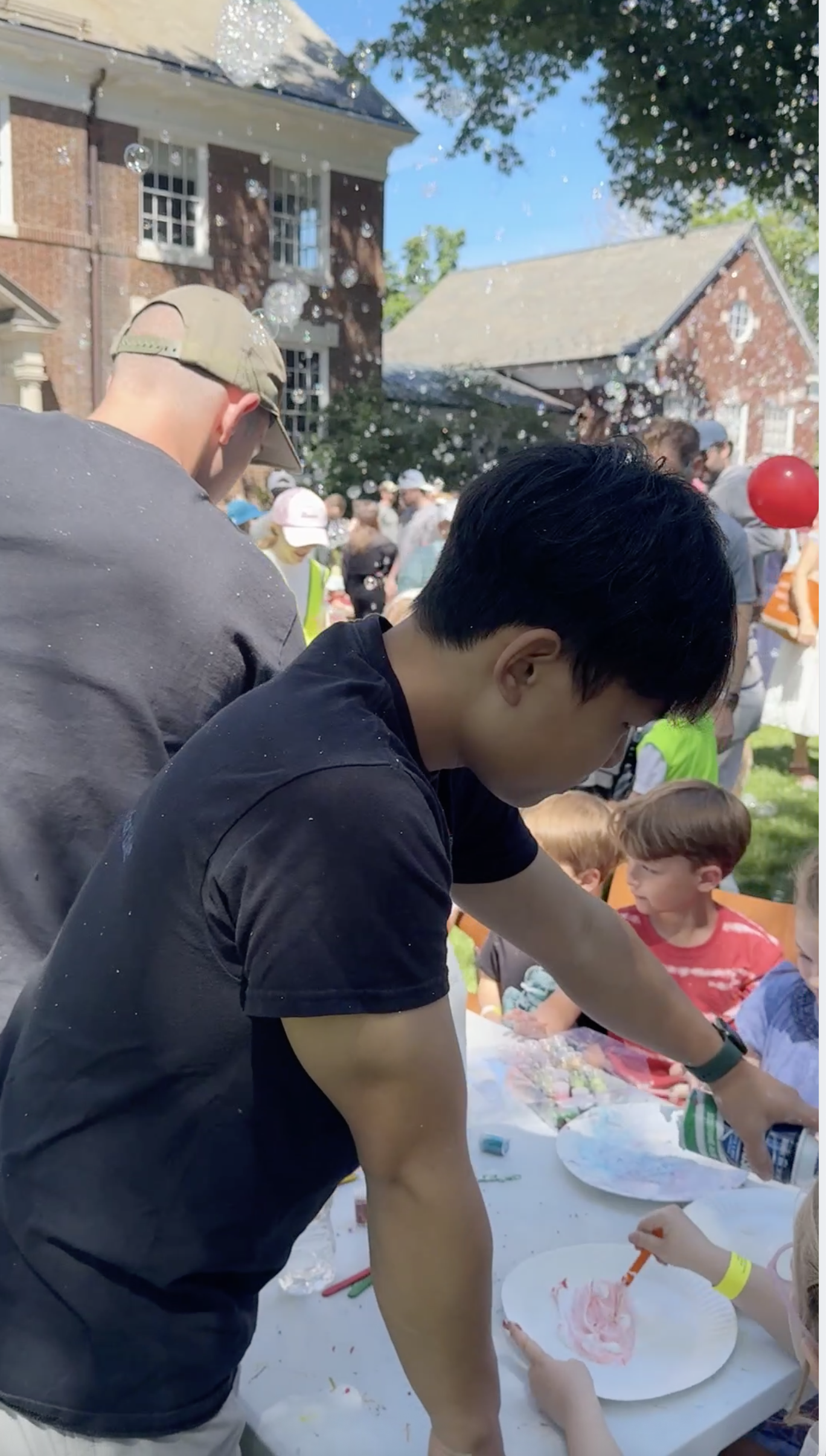 A Chemistry Club volunteer helping a child make slime at an outdoor Rye Vehicle Fair table.