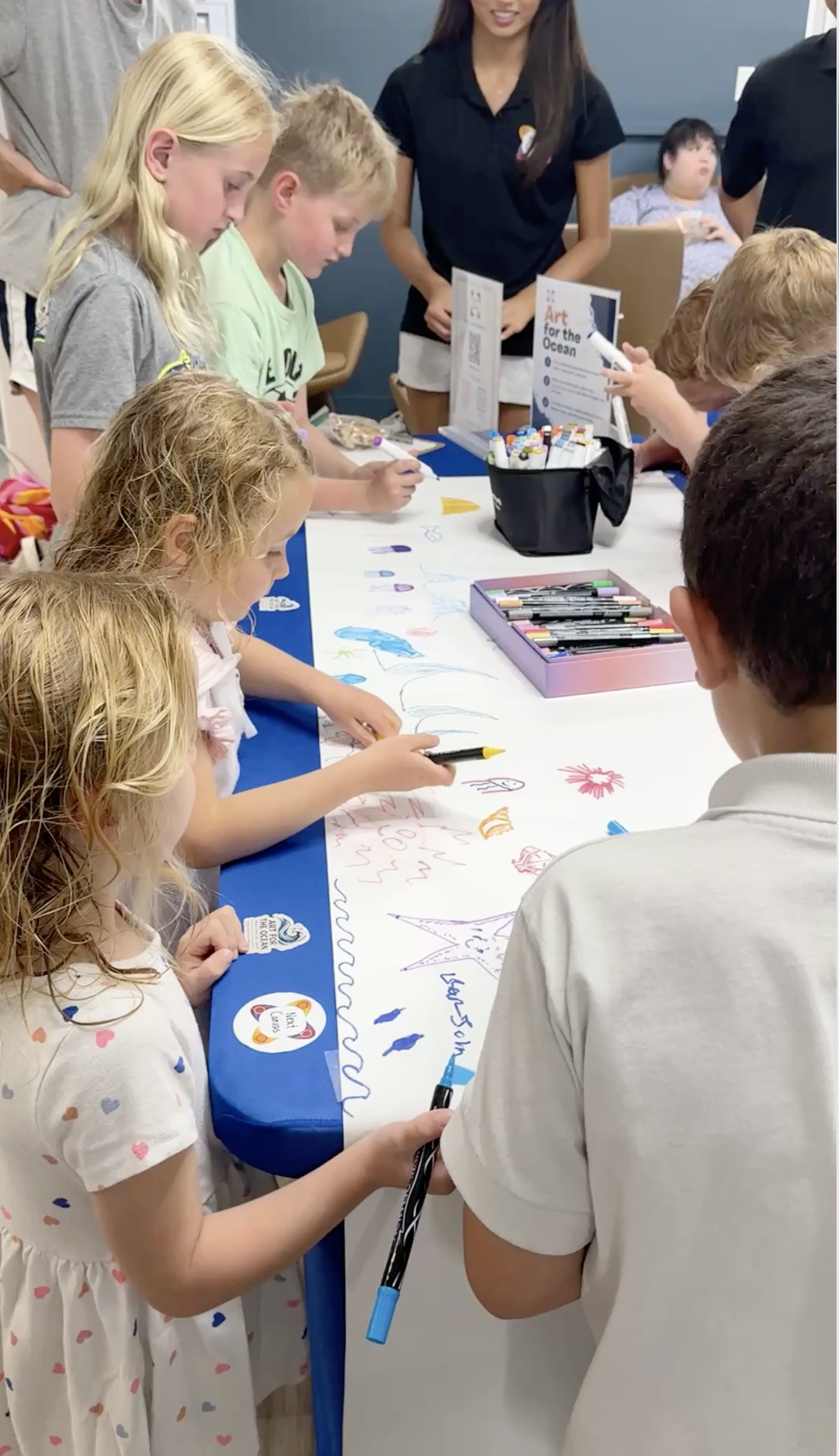 Children drawing together on a shared paper scroll at a NextCanvas ocean art event at Rye YMCA.