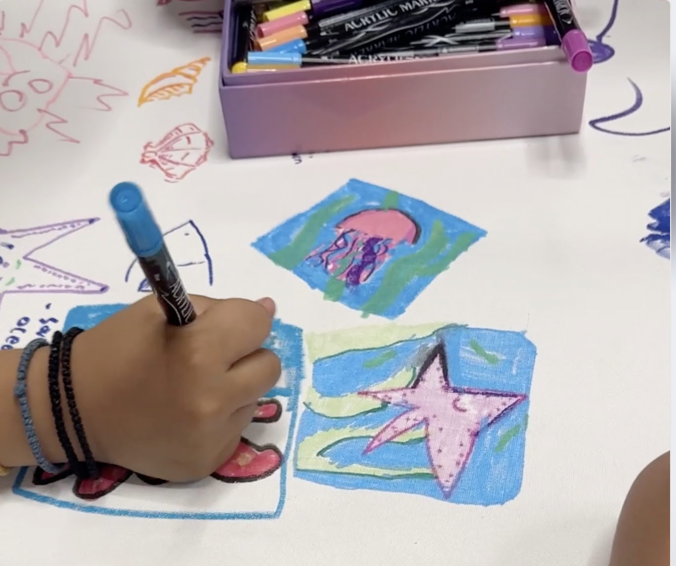 A participant coloring bright ocean-themed drawings on the community scroll at Rye YMCA.