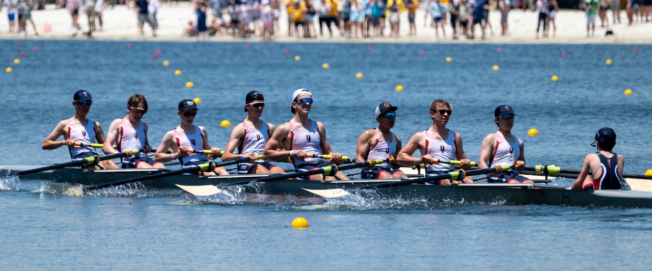 The RowAmerica Rye eight rowing together past spectators on the shore.