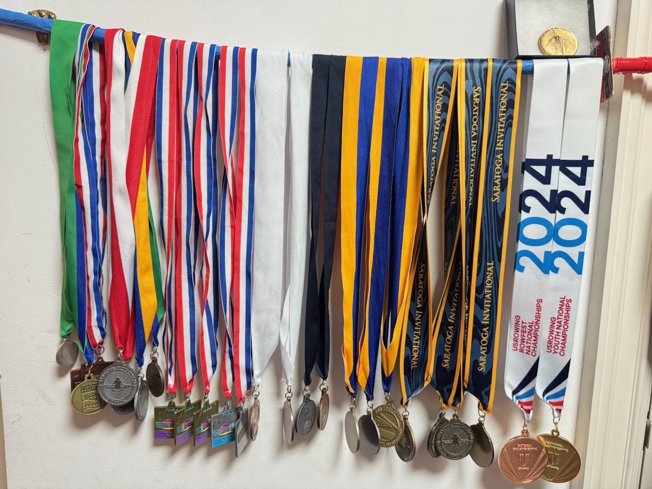 A collection of rowing medals hanging from colorful ribbons, including USRowing and Saratoga regatta medals.