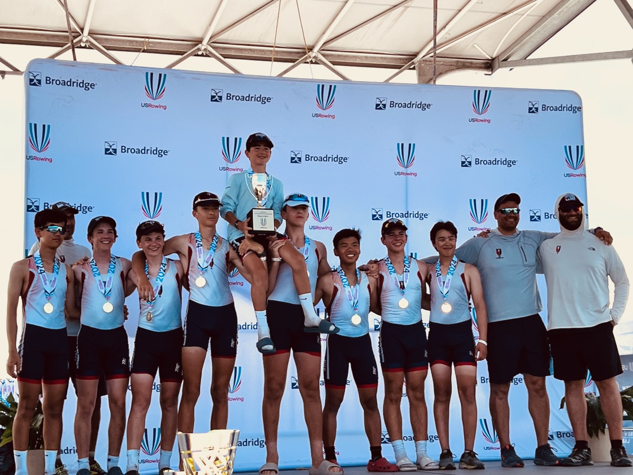The RowAmerica Rye U16 eight celebrating with gold medals, a trophy, and their coaches at the 2024 USRowing championships.